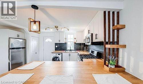 Kitchen featuring wood-finish countertops, white cabinetry with dark hardware, stainless steel appliances, and a black tile backsplash - 43 Adair Avenue S, Hamilton, ON - Indoor