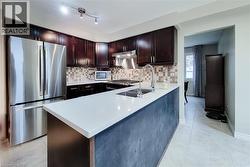 Kitchen featuring dark wood cabinetry, stainless steel appliances, a white countertop island with an integrated sink, and a tiled backsplash - 