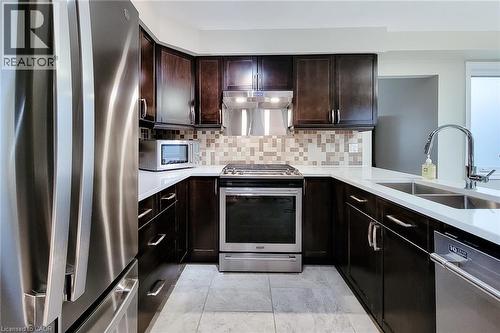 Kitchen featuring dark wood cabinetry, white countertops, stainless steel appliances, a mosaic tile backsplash, and light-toned tile flooring - 49 Ashwood Drive, Cambridge, ON - Indoor Photo Showing Kitchen With Stainless Steel Kitchen With Double Sink With Upgraded Kitchen