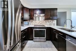 Kitchen featuring dark wood cabinetry, white countertops, stainless steel appliances, a mosaic tile backsplash, and light-toned tile flooring - 