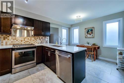 Modern kitchen featuring dark wood cabinetry, stainless steel appliances, a mosaic tile backsplash, and light-toned tile flooring - 49 Ashwood Drive, Cambridge, ON - Indoor Photo Showing Kitchen With Stainless Steel Kitchen With Double Sink With Upgraded Kitchen