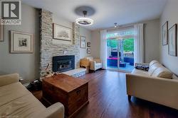 Living area featuring a floor-to-ceiling stacked stone fireplace with a black insert, wood-finish flooring, and a sliding glass door leading to an outdoor patio with a visible pink-toned hot tub - 