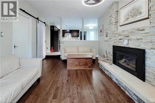 Living area featuring wood-finish flooring, a stacked stone fireplace with hearth, and a contemporary ceiling fixture - 49 Ashwood Drive, Cambridge, ON - Indoor Photo Showing Living Room With Fireplace