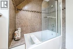 Bathtub with glass shower partition, featuring brown ceramic tile surround with a mosaic accent band, and chrome fixtures - 