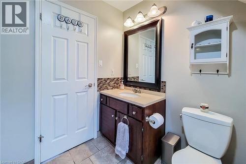 Bathroom featuring a dark wood-finish vanity with a light-toned countertop, a rectangular mirror, a three-light vanity fixture, and a mosaic tile backsplash - 49 Ashwood Drive, Cambridge, ON - Indoor Photo Showing Bathroom