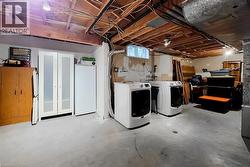 Basement laundry area featuring two front-loading machines, exposed ceiling joists, concrete flooring, and a small window - 