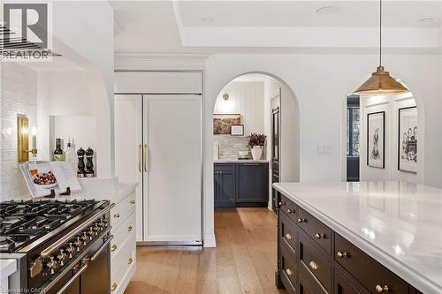 Gourmet kitchen featuring a professional-grade range, integrated panel-ready refrigerator, expansive center island with stone countertop, custom cabinetry, and arched doorways - 3081 Balmoral Avenue, Burlington, ON - Indoor Photo Showing Kitchen With Upgraded Kitchen