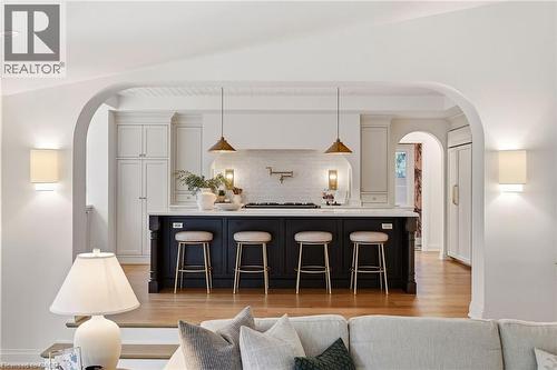Spacious kitchen featuring a large central island with seating, pendant lighting, white perimeter cabinetry, a built-in range hood, and light wood-finish flooring - 3081 Balmoral Avenue, Burlington, ON - Indoor Photo Showing Other Room