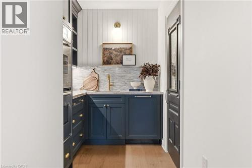 Compact kitchen space featuring deep blue cabinetry with brass hardware, a contrasting white shiplap accent wall, and wood-finish flooring - 3081 Balmoral Avenue, Burlington, ON - Indoor Photo Showing Kitchen