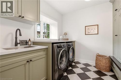 Laundry area featuring a utility sink with a dark bronze faucet, light green cabinetry, white countertops, and a checkerboard floor - 3081 Balmoral Avenue, Burlington, ON - Indoor Photo Showing Laundry Room