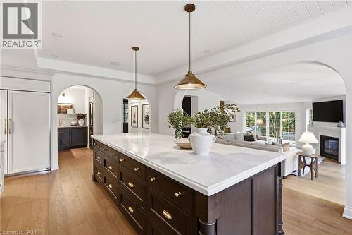 Expansive kitchen island featuring a light-toned countertop, dark wood-finish cabinetry, and brass-tone hardware - 3081 Balmoral Avenue, Burlington, ON - Indoor Photo Showing Kitchen With Fireplace