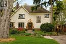 Stucco exterior residence featuring an arched wood-panel entry door, a stone pathway, a prominent chimney, and mature trees with established landscaping - 3081 Balmoral Avenue, Burlington, ON  - Outdoor 