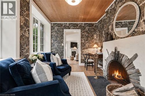 Living area featuring a stone fireplace with a hearth, wood-finish ceiling, patterned wall coverings, wood-finish flooring, and a multi-pane window - 3081 Balmoral Avenue, Burlington, ON - Indoor Photo Showing Other Room With Fireplace