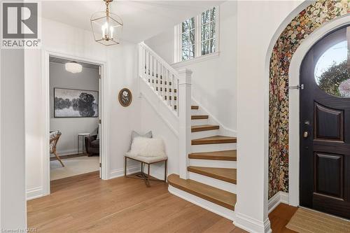 Entry foyer featuring light wood-finish flooring, a contemporary lantern-style chandelier, a dark wood entry door with an arched glass insert, and an elegant staircase with white risers and wood-finis - 3081 Balmoral Avenue, Burlington, ON - Indoor Photo Showing Other Room