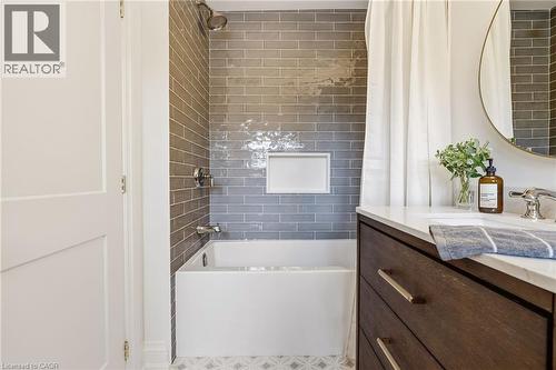 Bathroom featuring a built-in tub with subway tile surround, integrated shower niche, a dark wood-finish vanity with drawer storage, a white countertop, and patterned floor tile - 3081 Balmoral Avenue, Burlington, ON - Indoor Photo Showing Bathroom
