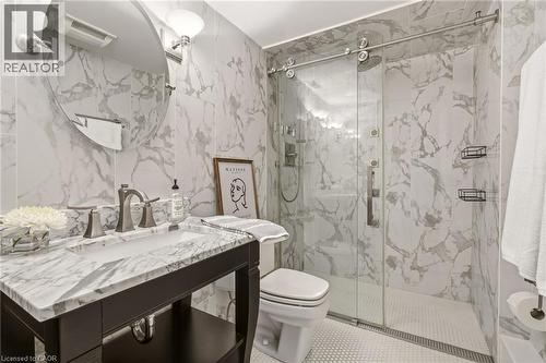 Bathroom featuring full-height marble-patterned tile, a dark wood-finish vanity with a marble-patterned countertop, a rectangular undermount sink, a frameless glass shower enclosure, and a walk-in sho - 3081 Balmoral Avenue, Burlington, ON - Indoor Photo Showing Bathroom