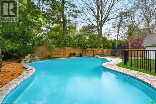 Freeform swimming pool featuring a waterfall, natural stone coping, full fencing, and surrounding mature trees - 3081 Balmoral Avenue, Burlington, ON - Outdoor With In Ground Pool With Backyard