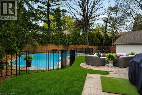 Private backyard oasis featuring a curved swimming pool with stone coping, surrounded by a black metal fence - 3081 Balmoral Avenue, Burlington, ON - Outdoor With In Ground Pool With Backyard