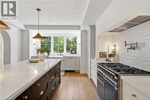 Gourmet kitchen featuring a large central island with a quartz countertop, a farmhouse sink beneath a multi-pane window, wood-finish flooring, a commercial-style range with a pot filler, and white shi - 3081 Balmoral Avenue, Burlington, ON - Indoor Photo Showing Kitchen With Upgraded Kitchen