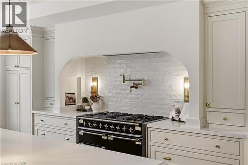 Gourmet kitchen featuring a professional-grade range, textured backsplash, integrated pot filler, custom cabinetry, and stone countertops - 3081 Balmoral Avenue, Burlington, ON - Indoor