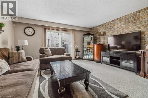 Living area featuring a textured stone-finish accent wall, light-toned carpeting, and a large sliding glass door with vertical blinds - 21 Lionshead Lookout, Brampton, ON - Indoor Photo Showing Living Room