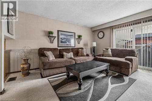Living area featuring carpet flooring, neutral wall tones, a built-in railing, and a sliding glass door with vertical blinds - 21 Lionshead Lookout, Brampton, ON - Indoor Photo Showing Living Room