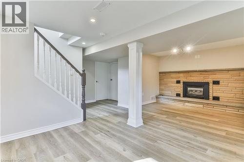 Spacious interior featuring wood-finish flooring, a stone-faced fireplace with hearth, recessed lighting, and a white baluster staircase with a dark wood-finish handrail - 38 Dunkirk Drive Unit# B, Hamilton, ON - Indoor Photo Showing Other Room With Fireplace