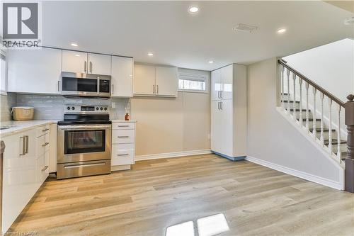 Contemporary kitchen area featuring stainless steel appliances, white flat-panel cabinetry, light-toned wood-finish flooring, recessed lighting, and a subway tile backsplash - 38 Dunkirk Drive Unit# B, Hamilton, ON - Indoor Photo Showing Kitchen