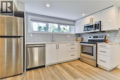 Kitchen featuring stainless steel appliances, white flat-panel cabinetry, light-toned countertops, a horizontal tile backsplash, and wood-finish flooring - 38 Dunkirk Drive Unit# B, Hamilton, ON - Indoor Photo Showing Kitchen With Stainless Steel Kitchen With Upgraded Kitchen