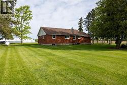Brick exterior with a brown shingle roof, surrounded by expansive green lawn, mature trees, and a visible outbuilding - 