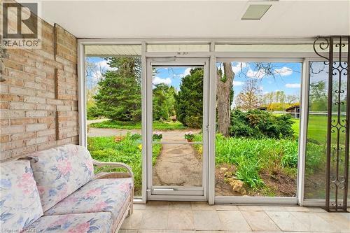 Enclosed porch featuring a brick wall, tiled flooring, expansive windows, and a glass door opening to a landscaped outdoor area - 10 Huisman Lane, Hamilton, ON 