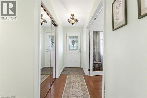 Entryway featuring wood-finish flooring, a decorative overhead light fixture, and a white door with a leaded glass insert - 10 Huisman Lane, Hamilton, ON 