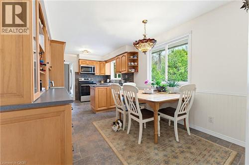 Kitchen featuring light wood cabinetry with glass-front accents, dark countertops, and stainless steel appliances including a microwave and range - 10 Huisman Lane, Hamilton, ON 