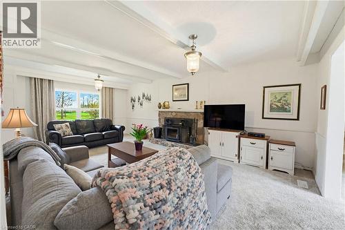 Living area featuring a stone fireplace with a wood stove insert, exposed ceiling beams, and light-colored carpet flooring - 10 Huisman Lane, Hamilton, ON 
