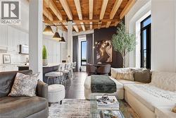 Open-concept living space featuring exposed wood beam ceilings, large black-framed windows, and dark wood-finish flooring - 