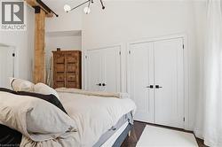 Interior space featuring a visible structural wood beam, multiple paneled doors with black hardware, wood-finish flooring, and a contemporary ceiling light fixture - 