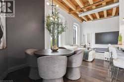 Open-concept living area featuring exposed wood beam ceilings, dark wood-finish flooring, and a modern light fixture - 