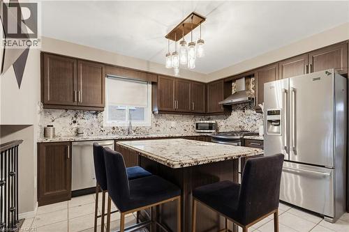 Modern kitchen featuring dark wood-finish cabinetry, stainless steel appliances, granite countertops, and a coordinating granite island with seating - 47 Hannah Crescent, Hamilton, ON - Indoor Photo Showing Kitchen