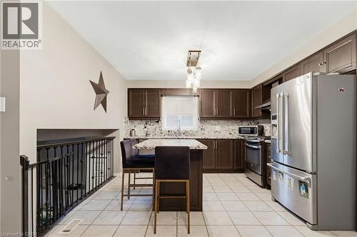 Kitchen featuring dark wood cabinetry, light-toned tiled flooring, and a central island with a contrasting countertop - 47 Hannah Crescent, Hamilton, ON - Indoor Photo Showing Kitchen