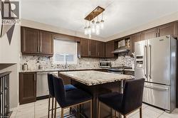 Modern kitchen featuring dark wood-finish cabinetry, stainless steel appliances, granite countertops, and a coordinating granite island with seating - 