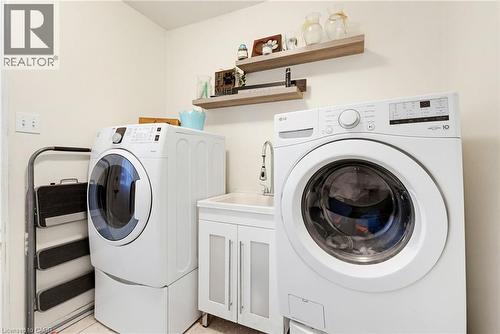 Dedicated laundry area featuring a white front-loading washer and dryer, a utility sink with a white vanity, and two floating wood shelves - 47 Hannah Crescent, Hamilton, ON - Indoor Photo Showing Laundry Room