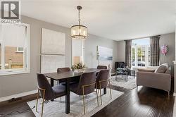 Open-concept living space featuring wood-finish flooring, a contemporary chandelier, large windows with roller shades, and neutral wall tones - 