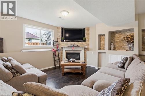 Living space featuring wood-finish flooring, a corner fireplace with a stone surround and mantle, a large window, and built-in shelving with stone accents - 47 Hannah Crescent, Hamilton, ON - Indoor Photo Showing Living Room With Fireplace