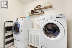 Dedicated laundry area featuring a white front-loading washer and dryer, a utility sink with a white vanity, and two floating wood shelves - 
