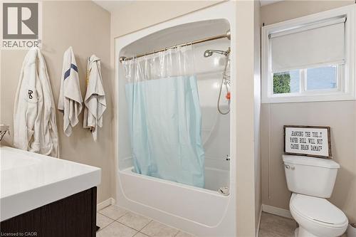 Bathroom featuring a tub/shower combination, a dark wood-finish vanity with an integrated white sink, a window with a roller blind, and light-toned floor tiles - 47 Hannah Crescent, Hamilton, ON - Indoor Photo Showing Bathroom