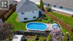 Fenced backyard featuring an oval above-ground pool with surrounding wood deck, a patio area with pergola, and a storage shed - 