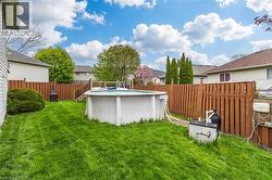 Expansive backyard featuring an above-ground pool with a surrounding wood deck, a wood privacy fence, and a decorative outdoor fire pit - 