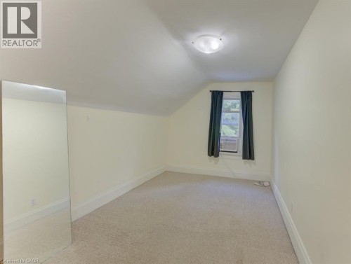 Carpeted flooring with sloped ceilings, featuring a single window and an overhead flush-mount light fixture - 10 Marshall Street, Waterloo, ON 