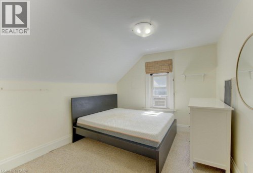 Sloped ceiling room featuring a window with a woven shade, wall-mounted light fixture, and carpet flooring - 10 Marshall Street, Waterloo, ON 