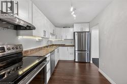 Kitchen featuring white cabinetry, stainless steel appliances, wood-finish flooring, undermount sink, and track lighting - 